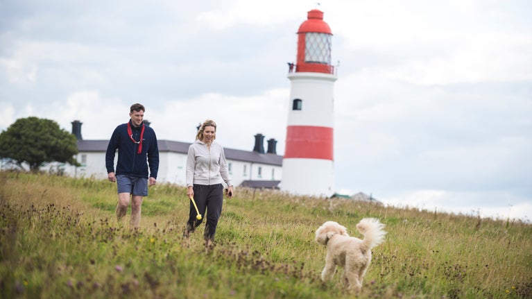 Two visitors walk their dog along the coastline in front of Souter Lighthouse in Tyne and Wear